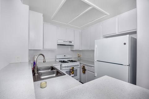 A white kitchen with a sink, stove, and refrigerator.