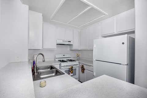 A white kitchen with a sink, stove, and refrigerator.