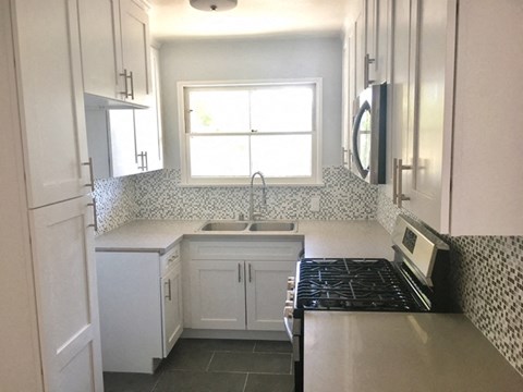 a small kitchen with white cabinets and a stove and a window
