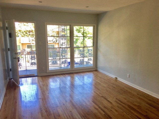 an empty living room with a wooden floor and a door to a balcony