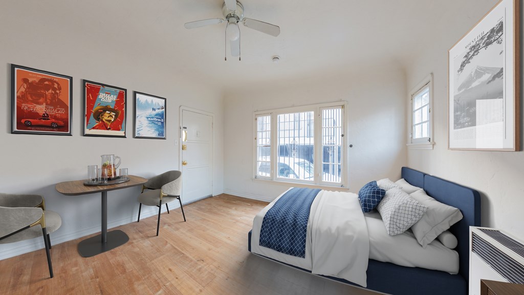 A bedroom with a bed, a table and chairs, and a ceiling fan.