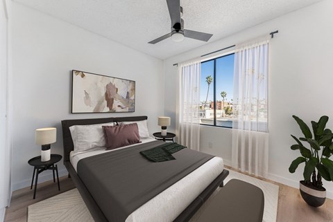 A bedroom with a large bed, a ceiling fan, and a view of the outside through the window.