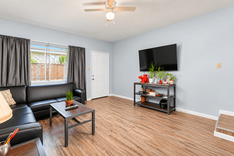 A living room with a black couch, a coffee table, and a flat screen TV mounted on the wall.