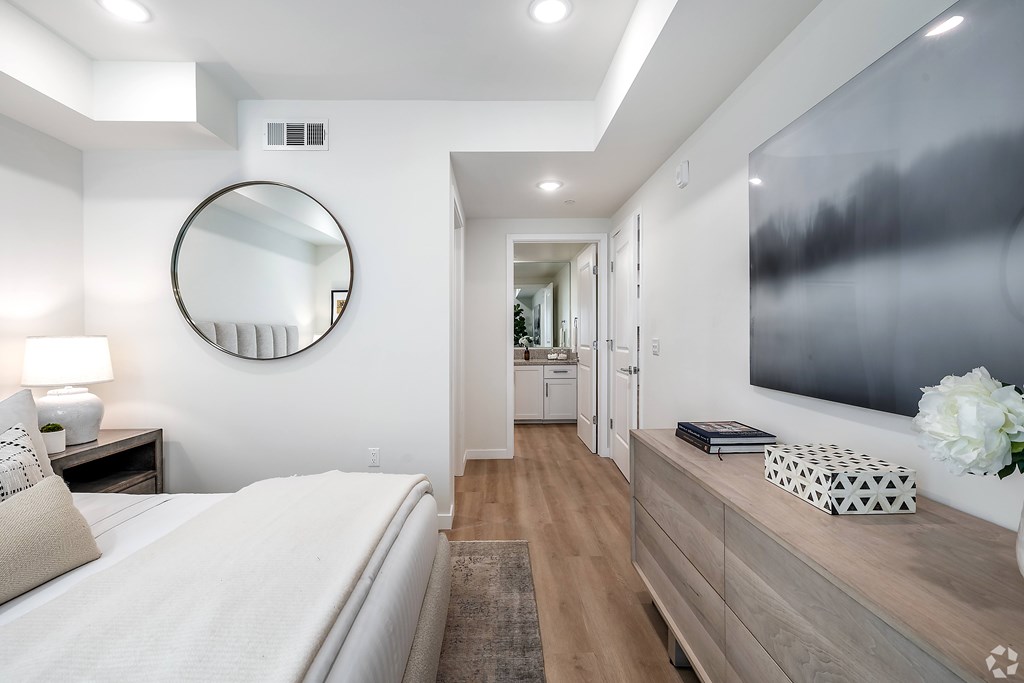 A bedroom with a large bed, a round mirror, and a tv on the wall above a dresser.