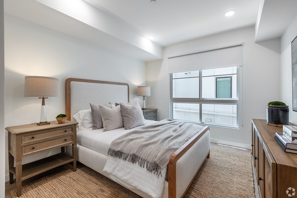 A bedroom with a large bed, a nightstand, and a window.