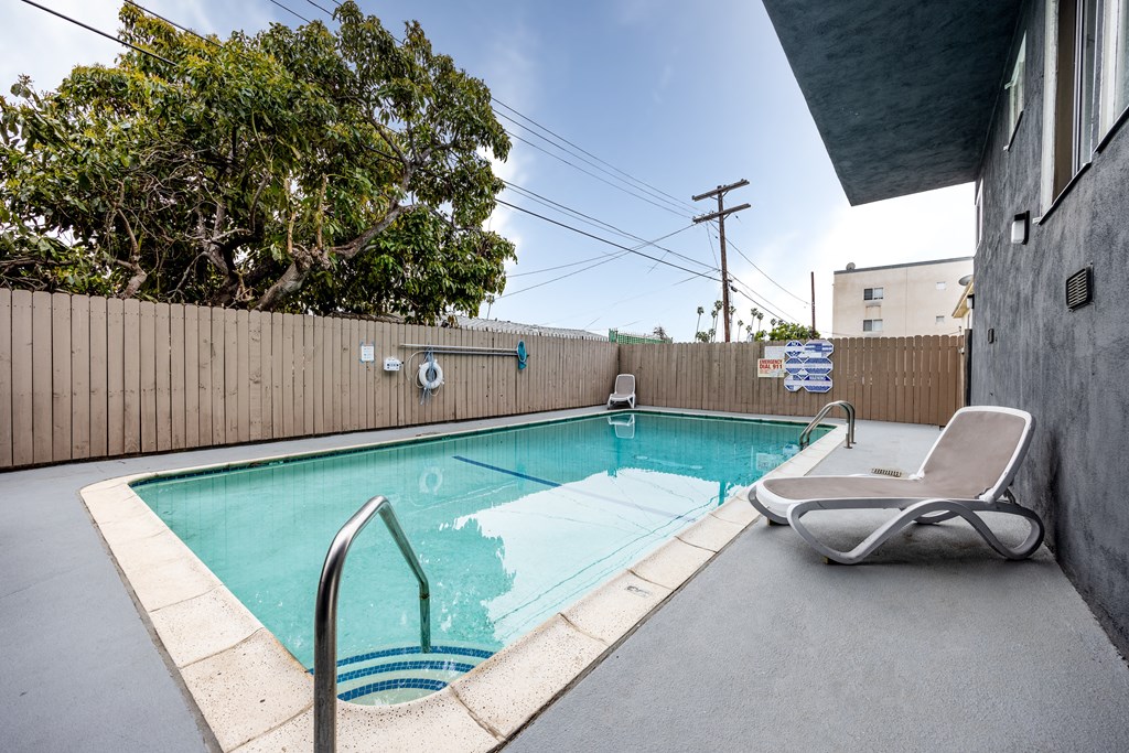 a swimming pool with a chaise lounge chair and a privacy fence with trees in the background