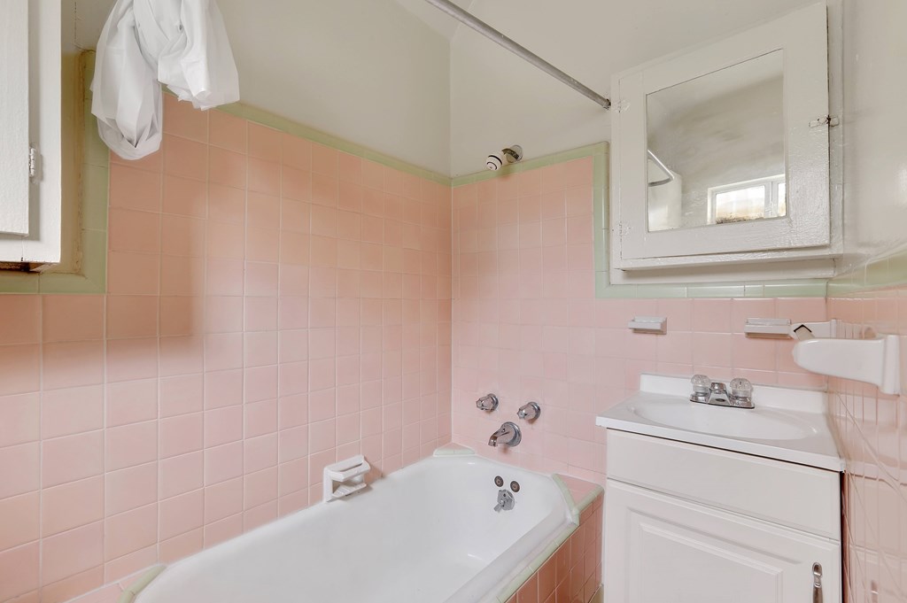 A white bathtub is in a bathroom with pink tiles.