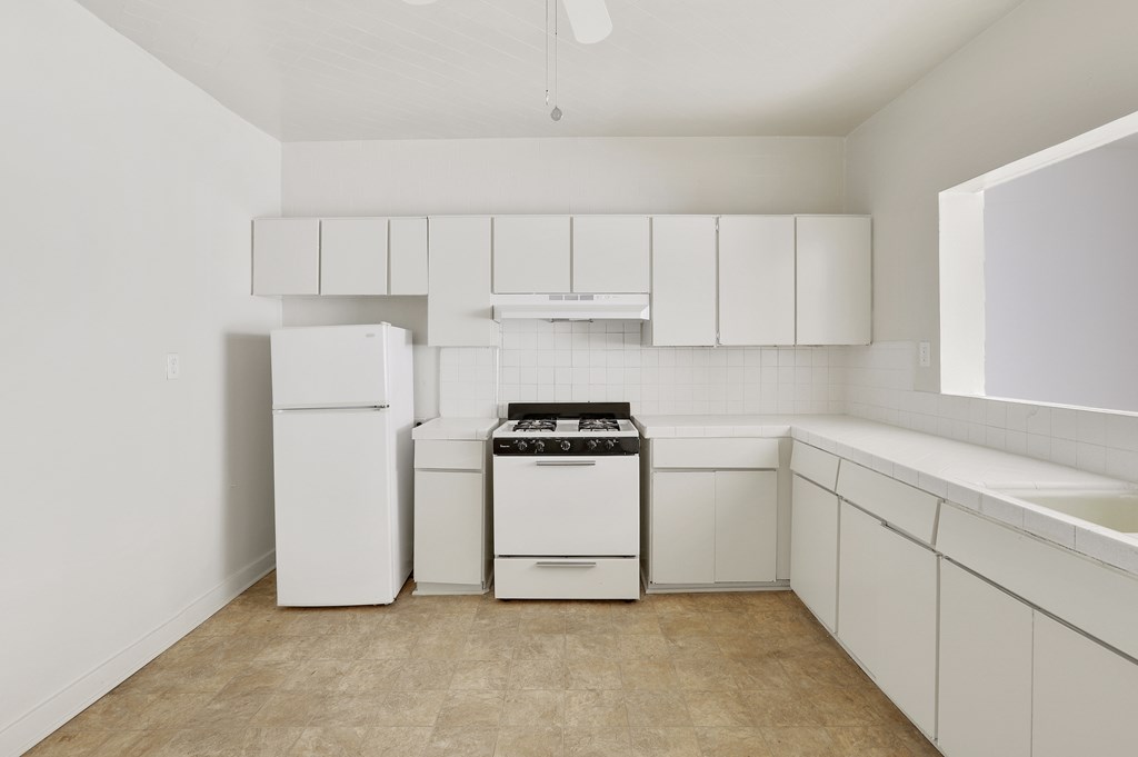 A white kitchen with a stove, refrigerator, and cabinets.
