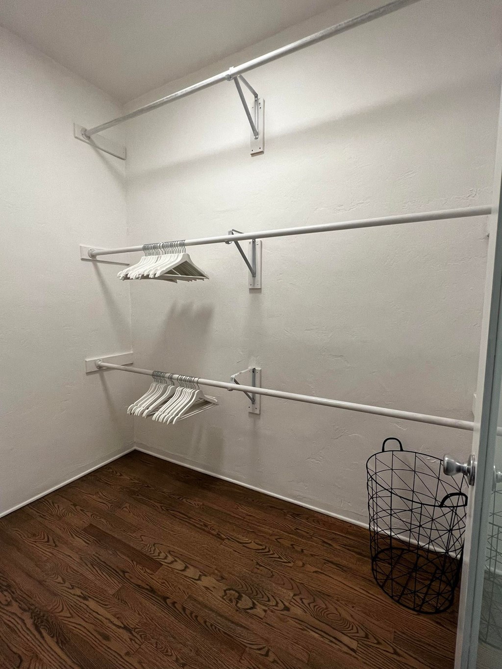 a walk in closet with white walls and a wood floor