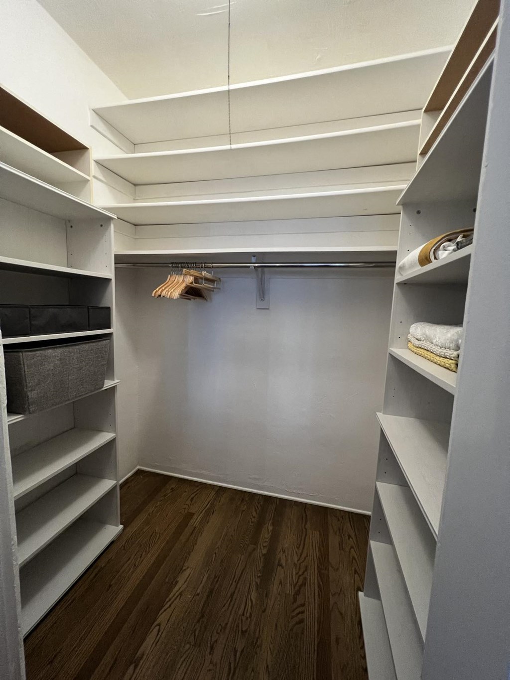 a walk in closet with white shelves and a wood floor