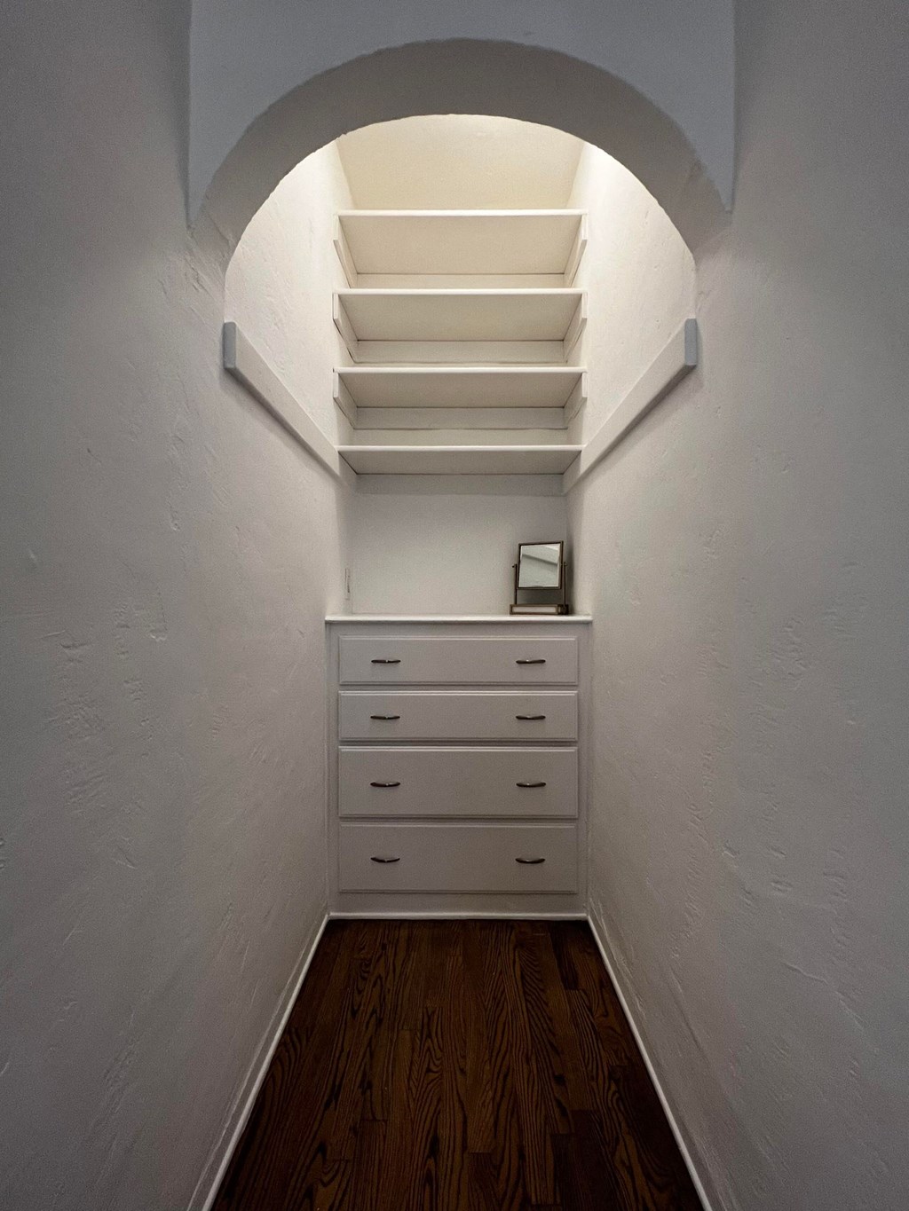 a small closet with white drawers and an arched ceiling