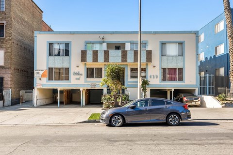 A grey car is parked in front of a multi-story building.