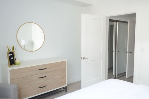 A white bedroom with a round mirror and a white dresser.