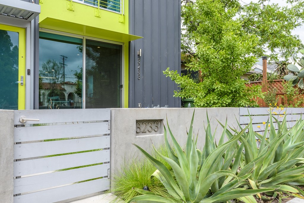 the front of the house is painted yellow and gray and has a fence and plants