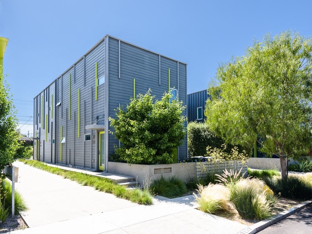 a modern building with greenery and a sidewalk in front of it