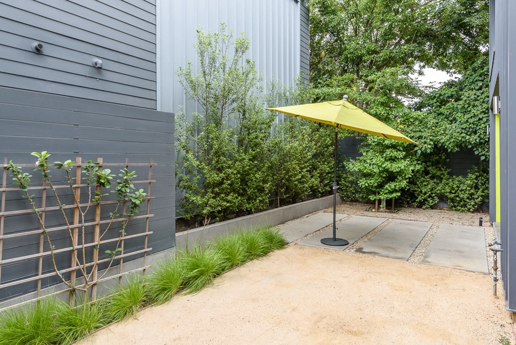 a patio with a yellow umbrella and a fence and plants