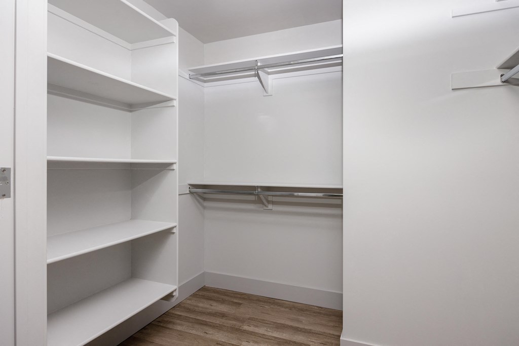 a walk in closet with white walls and shelves and a wood floor