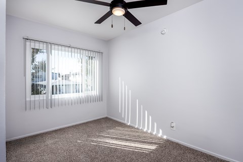 A room with a ceiling fan and a window with blinds.