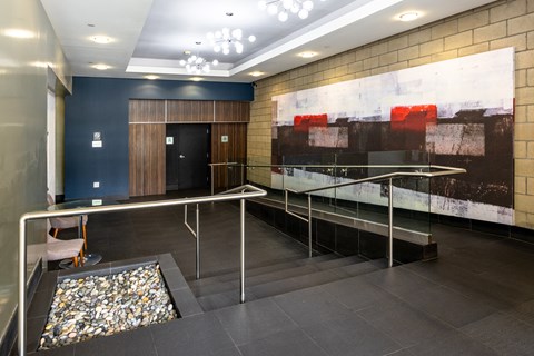 a lobby with a large painting on the wall and a staircase with glass railing