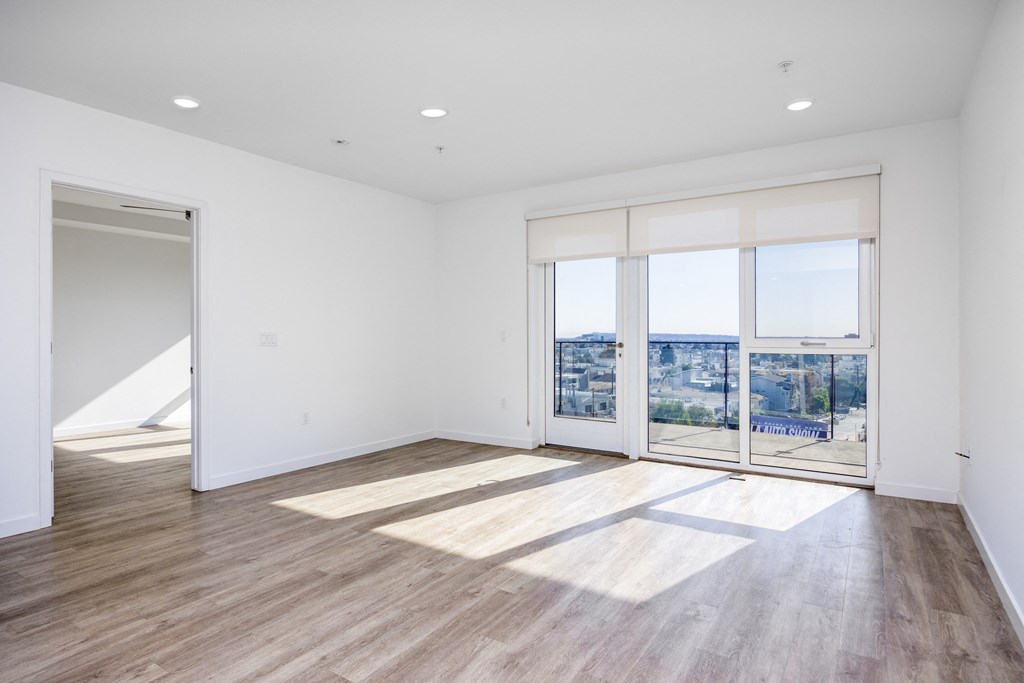 a living room with white walls and wooden floors and a door to a balcony
