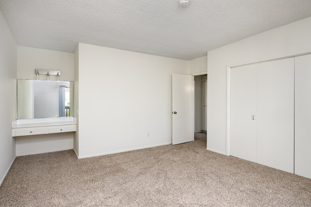 a bedroom with white walls and carpet and a bathroom with a sink and a mirror