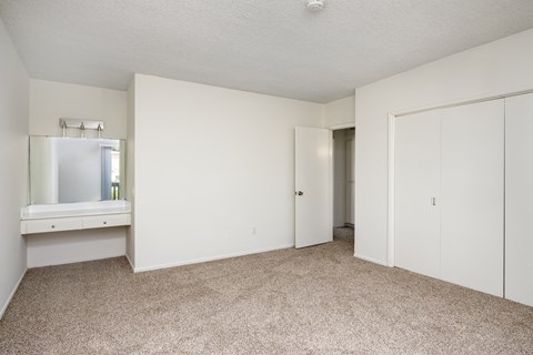 a bedroom with white walls and carpet and a bathroom with a sink and a mirror