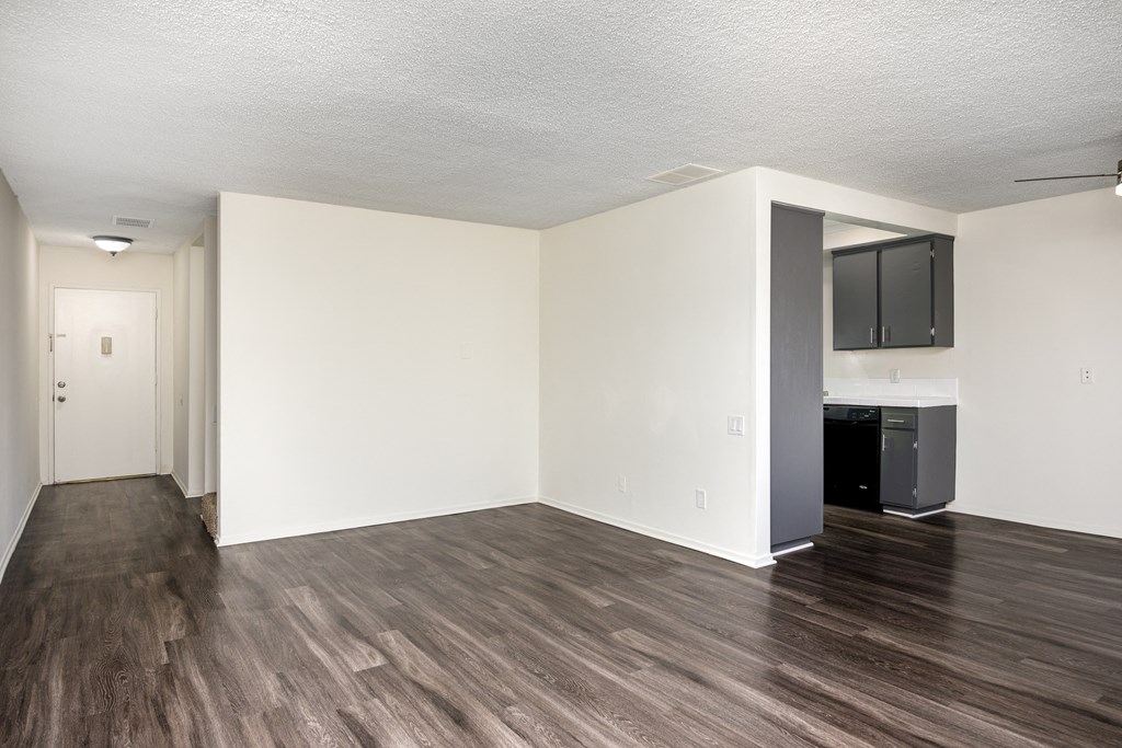 the living room and kitchen of an apartment with hardwood floors and white walls