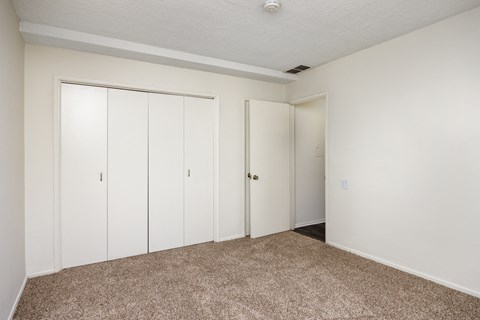 an empty bedroom with white closets and carpeting