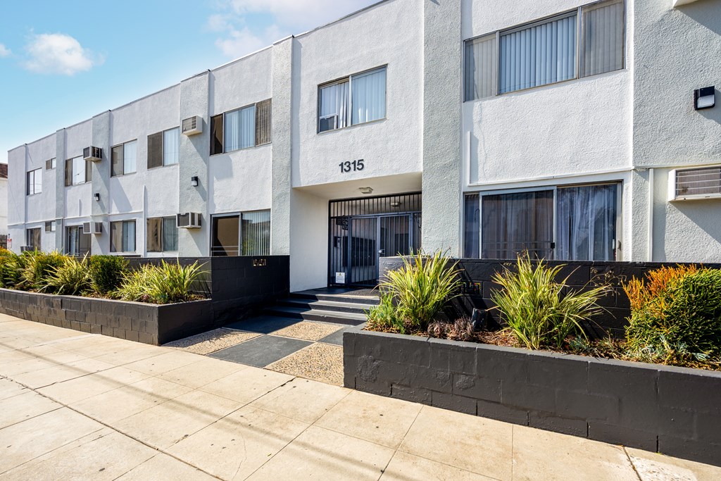 an apartment building with a sidewalk and plants in front of it