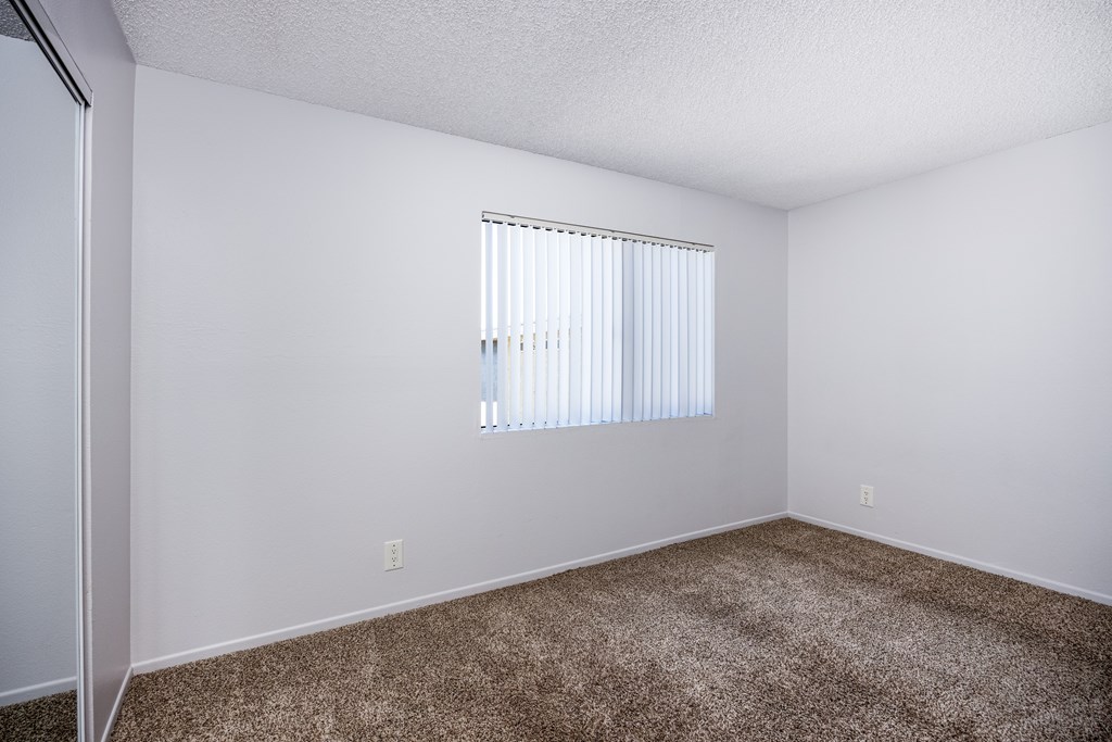 A room with a carpeted floor and a window with blinds.