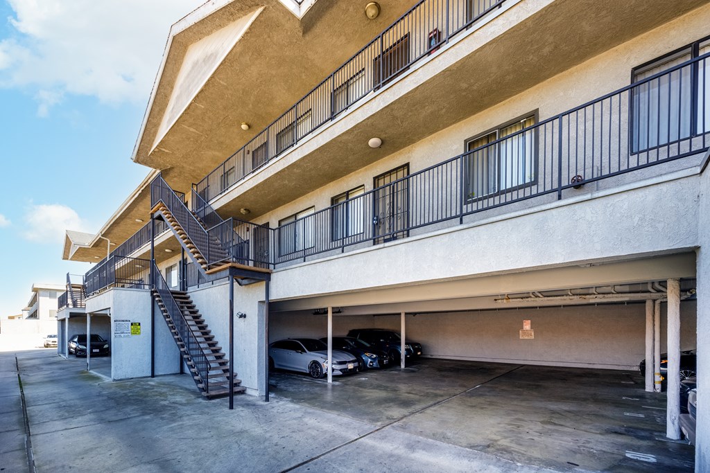 A car is parked in a garage under a building with a balcony.