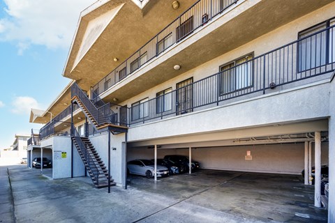 A car is parked in the garage of a building with a staircase leading to the upper floor.