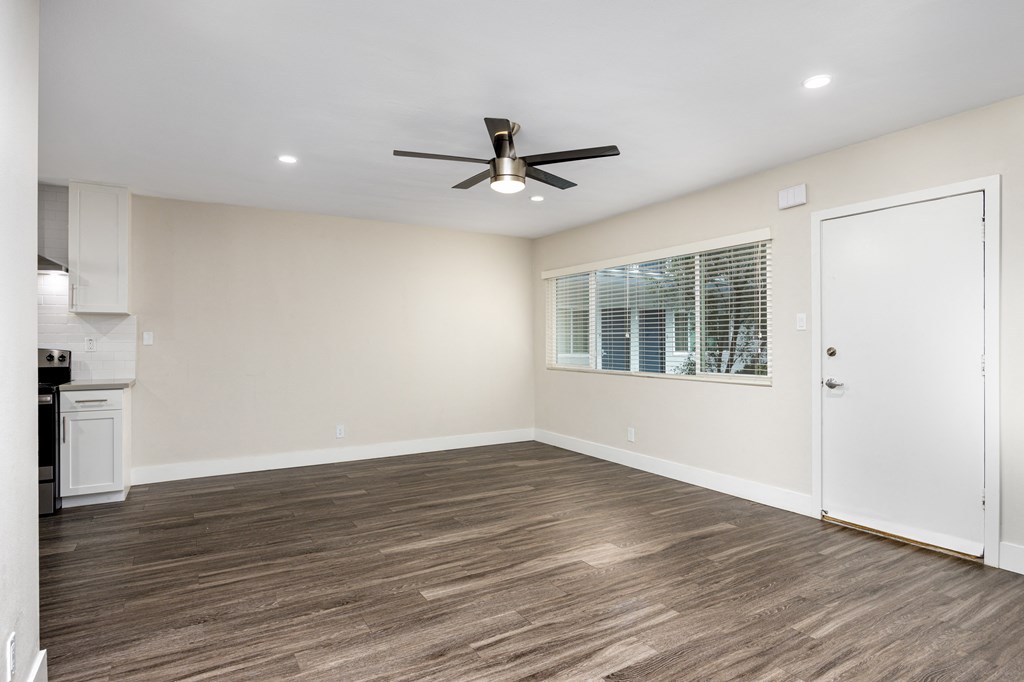 an empty living room with a ceiling fan and a kitchen
