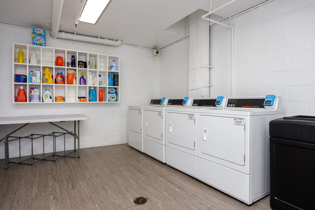 a laundry room with four washers and dryers and a table with a shelf