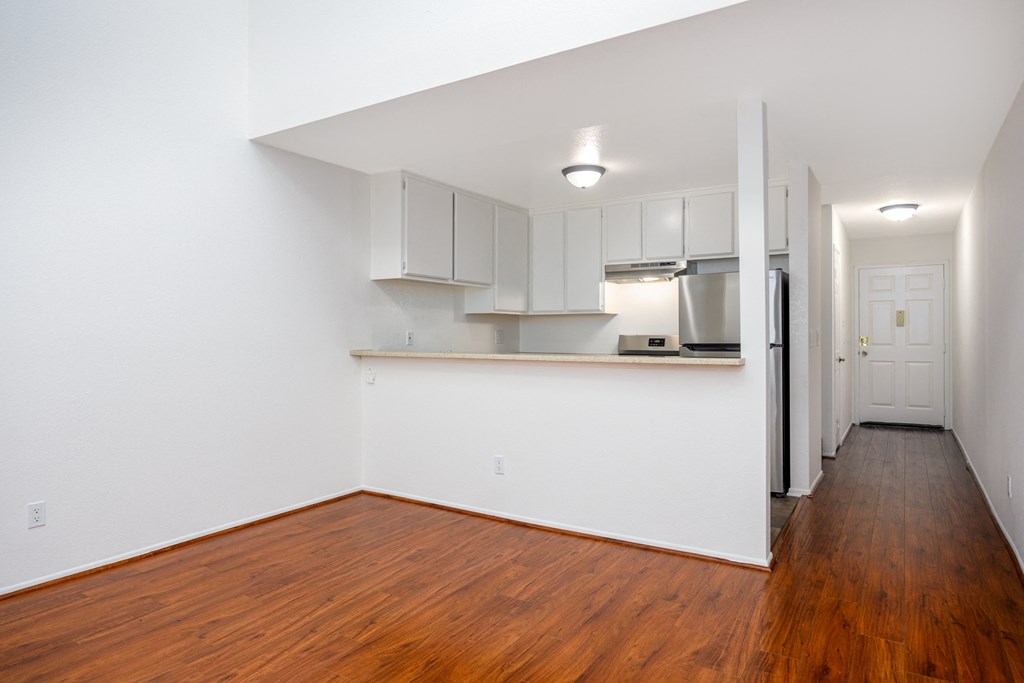 a living room with a hard wood floor and a kitchen with white cabinets