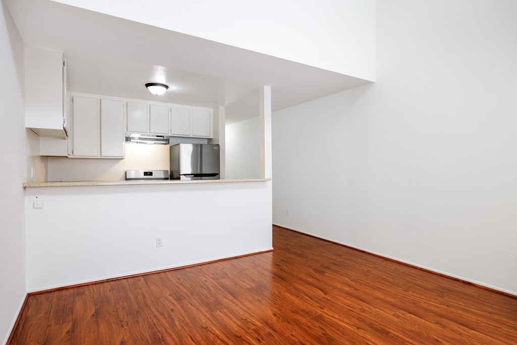 an empty living room with wood flooring and a kitchen