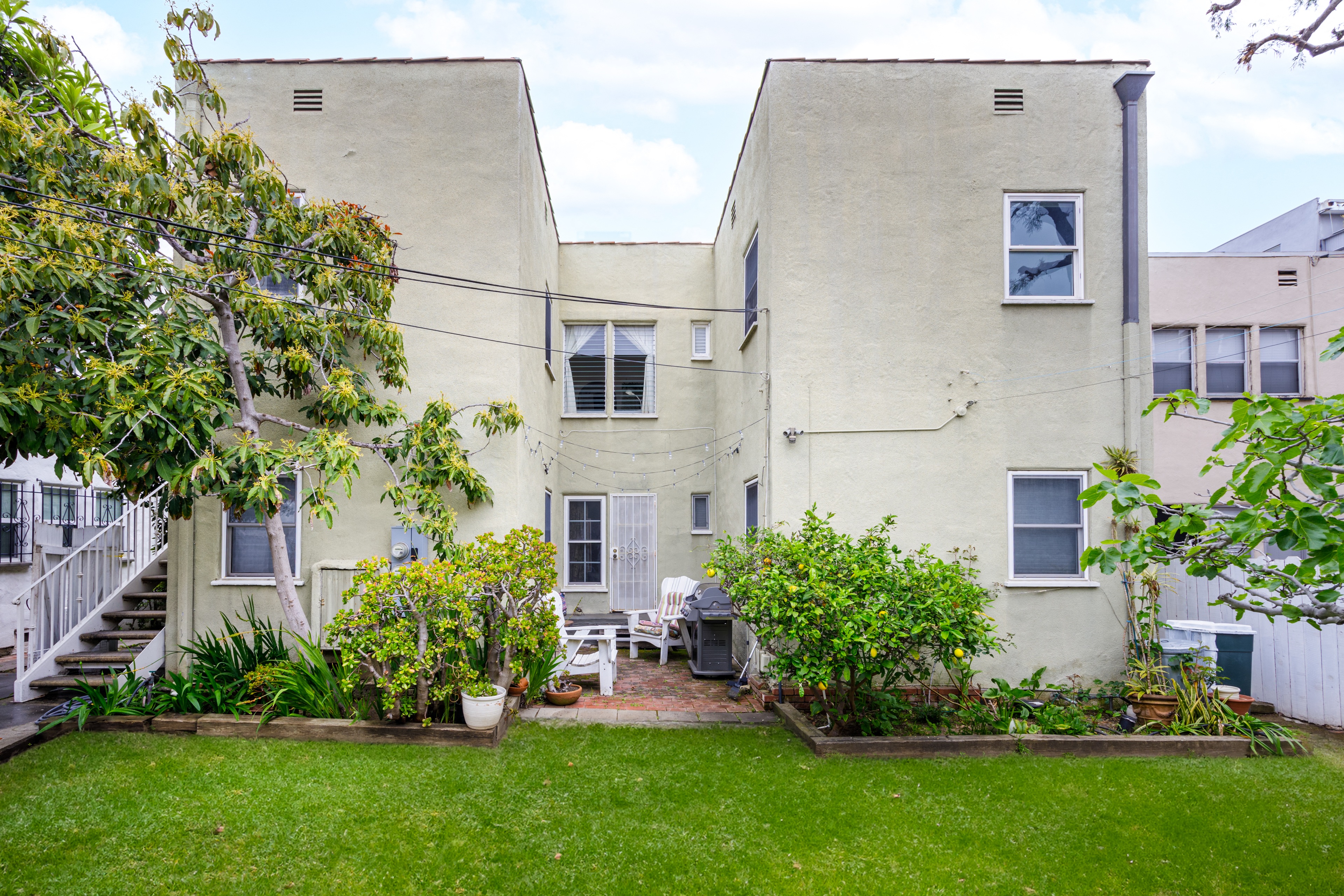 the backyard of a white apartment building with a lawn and plants