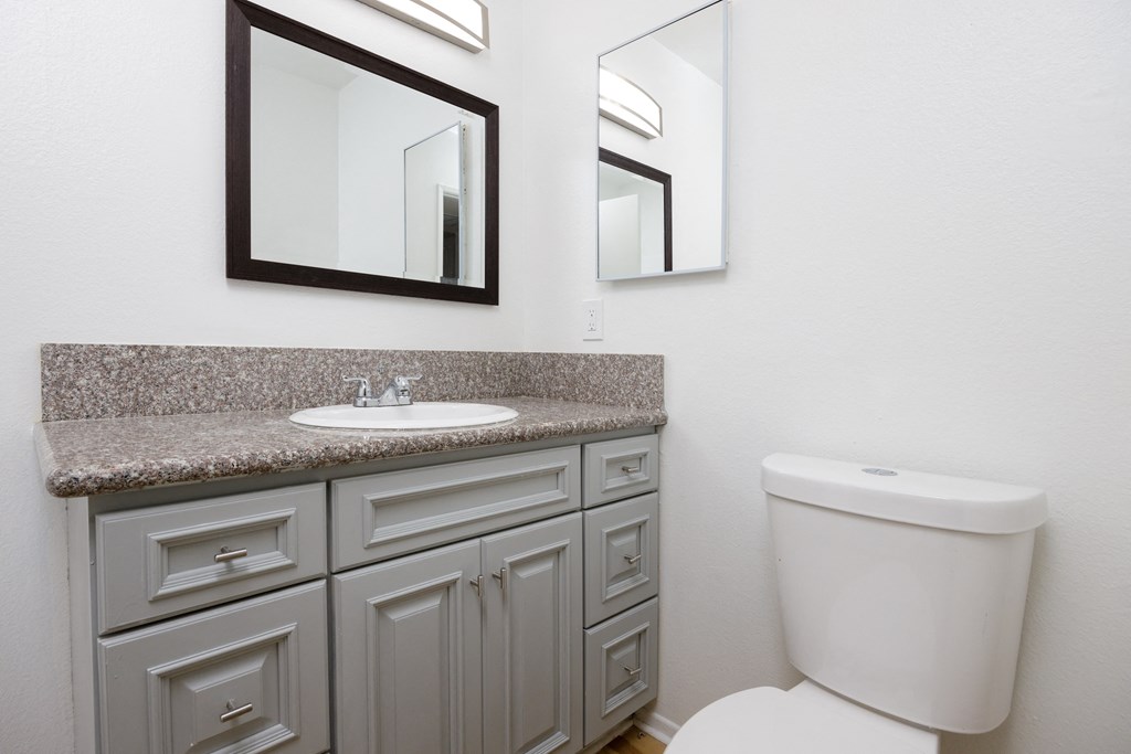 a bathroom with a sink and a toilet and two mirrors