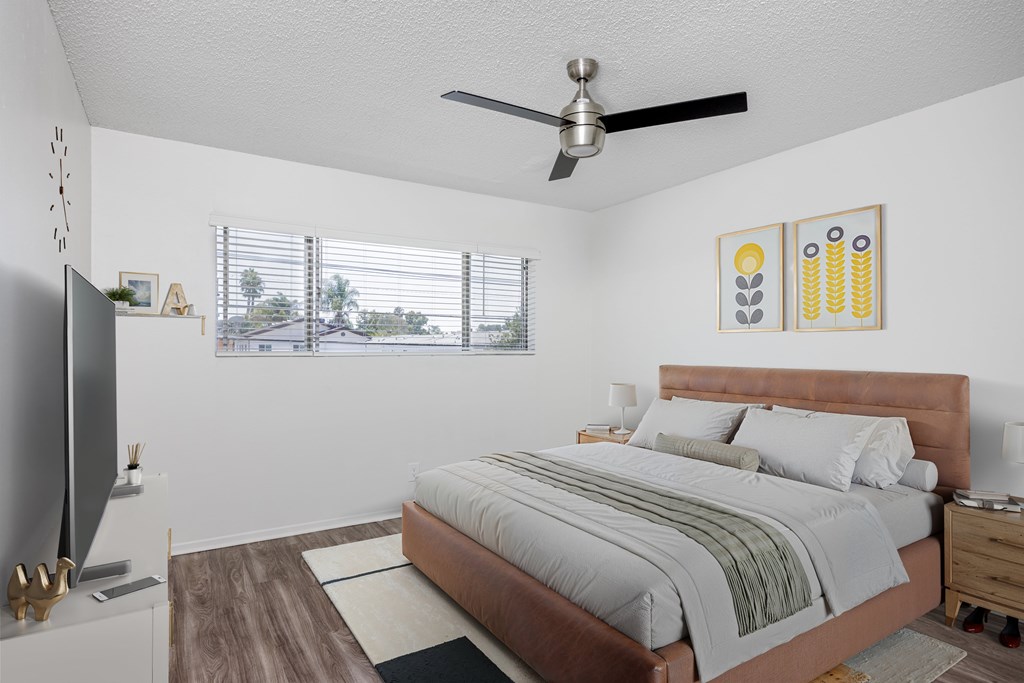 A bedroom with a bed, a television, and a ceiling fan.