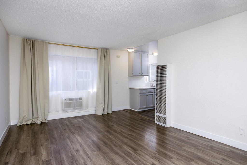 the living room and kitchen of an apartment with wood flooring and a window