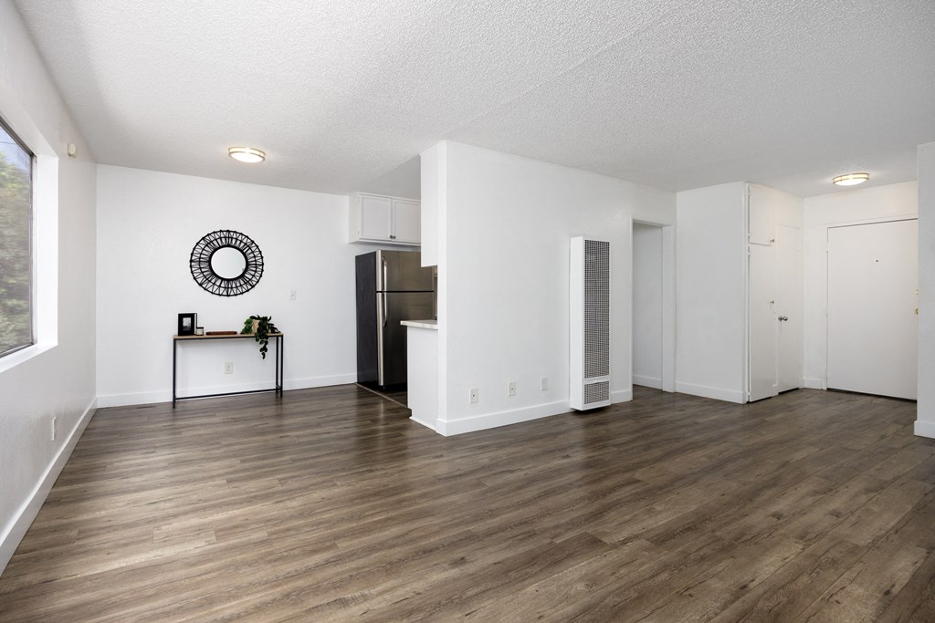 the living room and kitchen of an apartment with white walls and wood flooring