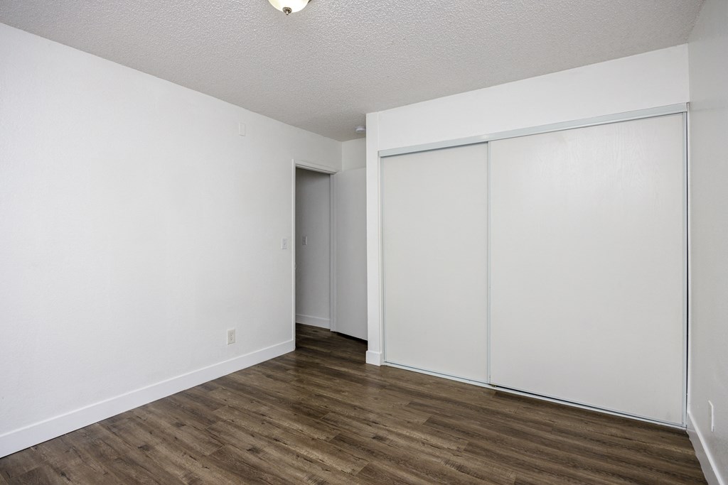 a bedroom with white walls and wood flooring and a closet