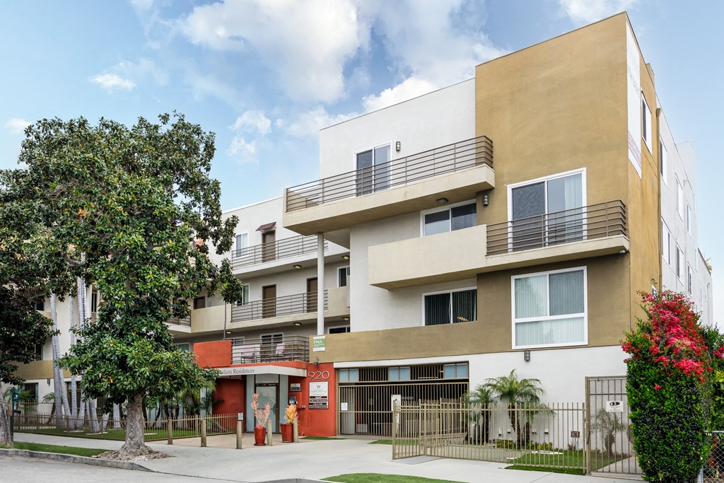 an apartment building with a sidewalk and a tree in front of it