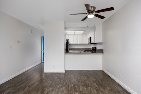 an empty living room with a ceiling fan and a kitchen