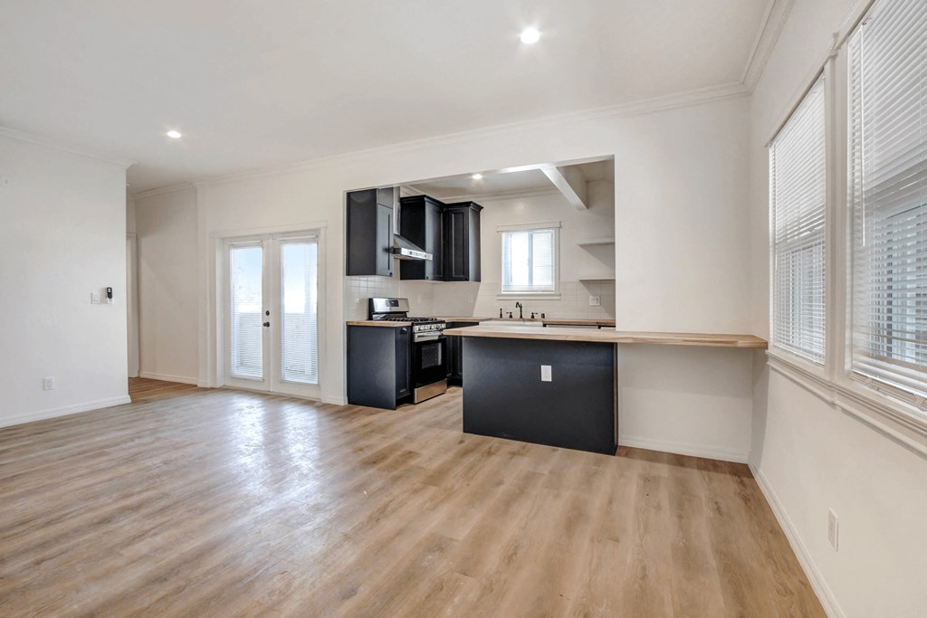 the living room and kitchen of an apartment with wood flooring and a large window