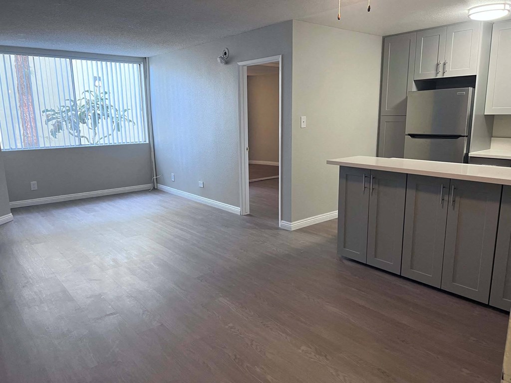 an empty living room with a kitchen and a large window