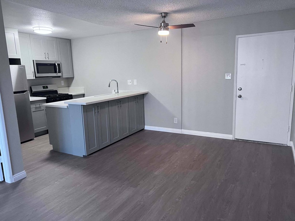 an empty living room with a kitchen and a ceiling fan