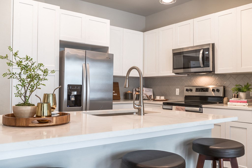 College Station, TX Apartments for Rent - Caprock Crossing - Modern Kitchen with Stainless Steel Appliances, Grey Tile Backsplash, and Modern Wood Cabinets