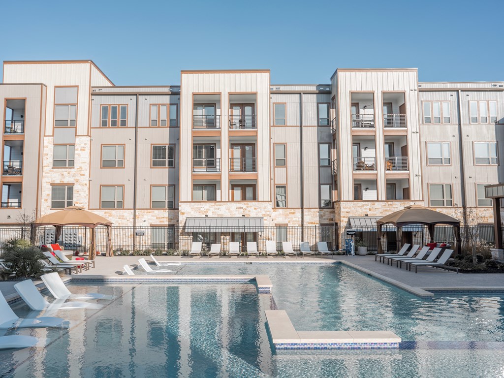 College Station, TX Apartments - Exterior View of Caprock Crossing Apartments Building Surrounded By Lush Landscaping with View of Outdoor Lounge