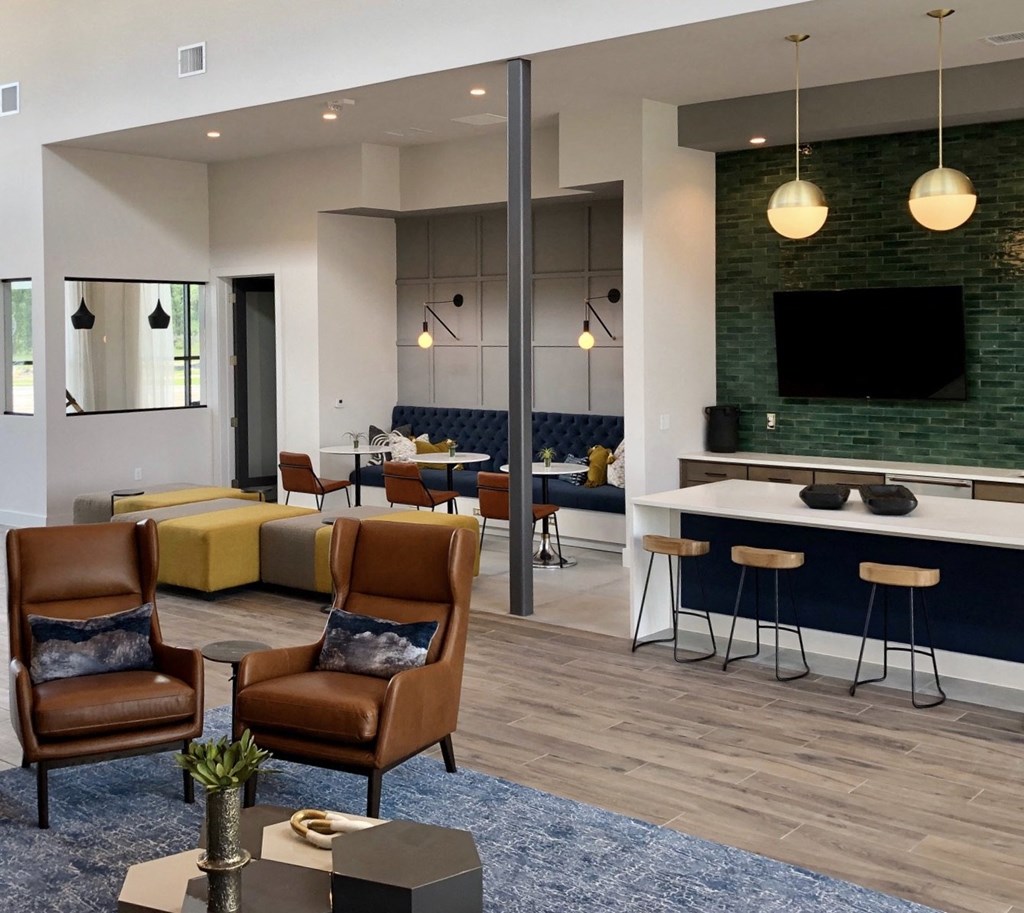 Apartments for Rent in College Station TX - Caprock Crossing - Clubhoue with a TV, Couch Seating, a Table with Chairs, Cushioned Booths, Green Tile Design, and Hanging Lights
